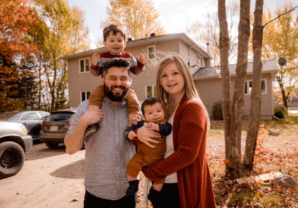 Young Couple With Young Children Standing in front of Home in Fall